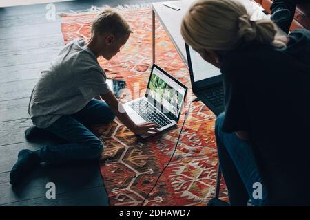 High angle view of woman looking at boy using laptop by coffee table in living room at home Stock Photo