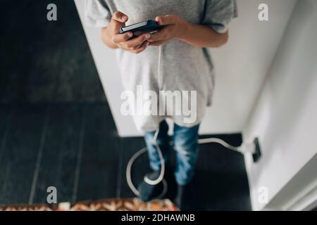 Low section of boy using smart phone while standing in room at home Stock Photo