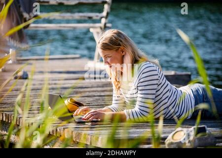 Woman lying on front while working over laptop at pier during summer Stock Photo