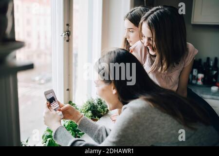 Friends looking at girl photographing through smart phone from window Stock Photo