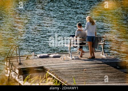 Woman standing by man working on laptop while female executive standing on wooden pier against lake Stock Photo