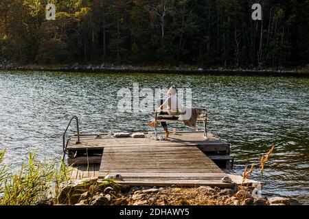 Thoughtful man with laptop sitting on bench over jetty against lake Stock Photo