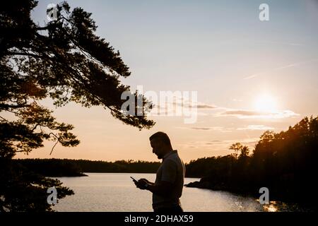 Silhouette man using smart phone while standing at lake during sunset Stock Photo