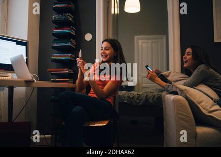 Happy friends using phone and talking while sitting at home Stock Photo