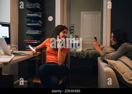Friends using phone and talking while sitting at home Stock Photo