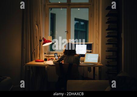 Girl using laptop and computer while sitting at illuminated desk Stock Photo