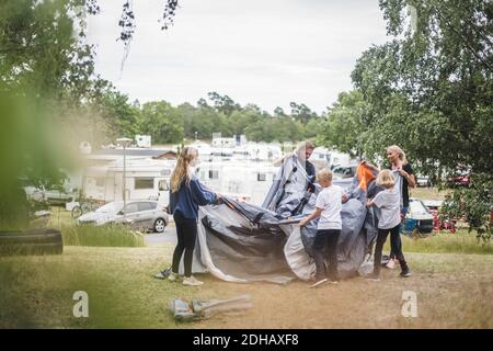 Family pitching tent together at camping site during summer vacation Stock Photo