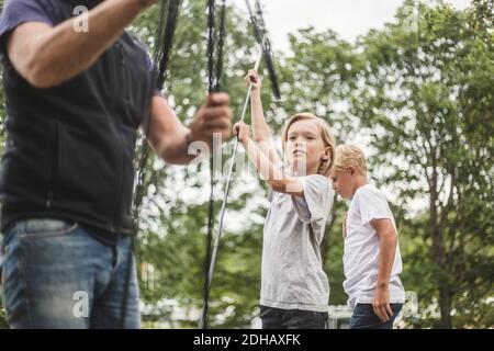 Siblings assisting father in making tent at camping site Stock Photo