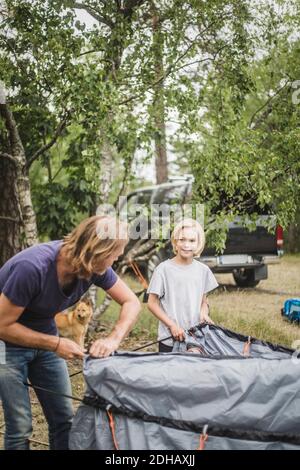 Father and daughter talking while pitching tent at camping site Stock Photo