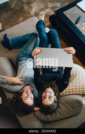 High angle view of smiling girls using laptop while resting on sofa at home Stock Photo