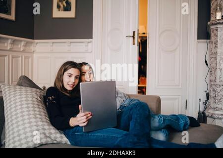 Smiling girls using laptop while resting on sofa at home Stock Photo