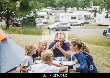 Happy family talking while having food together at table by tent Stock Photo