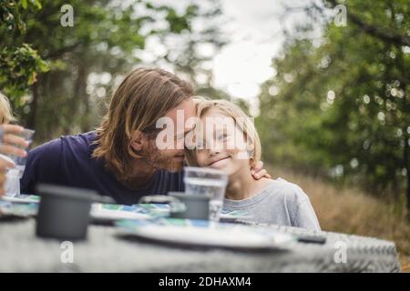 Affectionate father embracing daughter at table in campsite Stock Photo