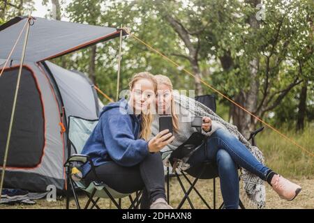 Mother and daughter taking selfie on smart phone while having coffee in campsite Stock Photo