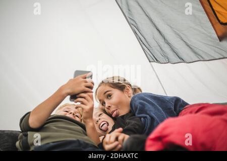 Siblings making face while taking selfie in tent Stock Photo
