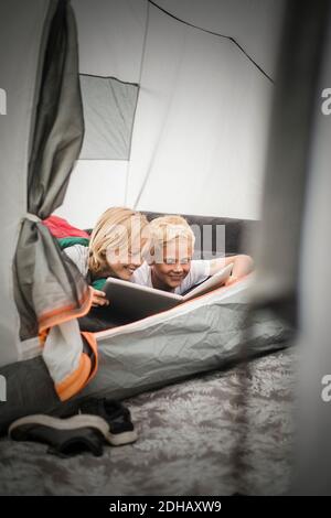 Smiling siblings using digital tablet while lying in tent at camping site Stock Photo