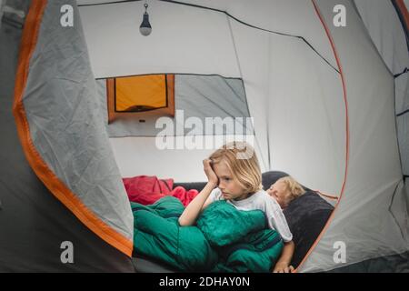 Girl rubbing eyes while waking up by brother in tent during camping Stock Photo