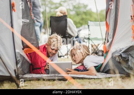 Siblings talking while using digital tablet in tent at campsite Stock Photo