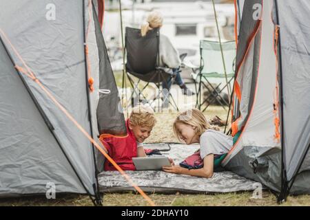Smiling sister showing digital tablet to brother in tent at campsite Stock Photo