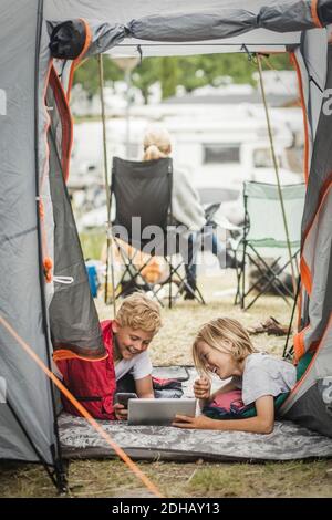 Happy brother and sister using digital tablet to brother in tent at campsite Stock Photo