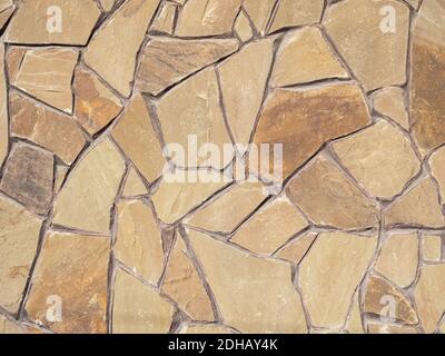 Exterior beige brown wall with decorative masonry made of many pieces of various shapes and sizes Stock Photo