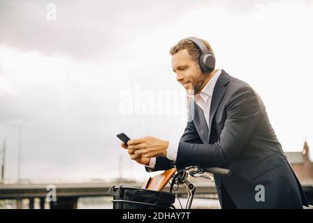 Businessman using mobile phone while leaning on bicycle handle against sky Stock Photo