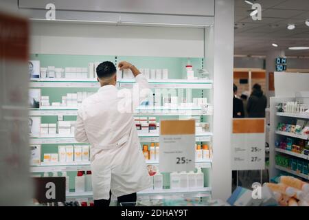 Rear view of male pharmacist arranging medicines on rack at store Stock Photo