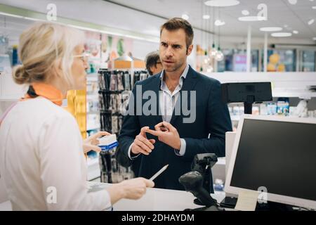 Mature man explaining to female pharmacist standing at checkout in medical store Stock Photo