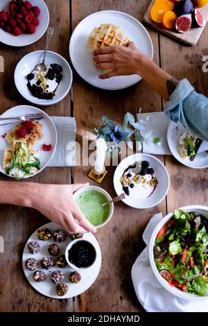 Cropped hands of couple having food at table while sitting by wall Stock Photo