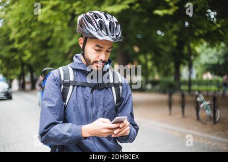 Food delivery man using mobile phone on street in city Stock Photo