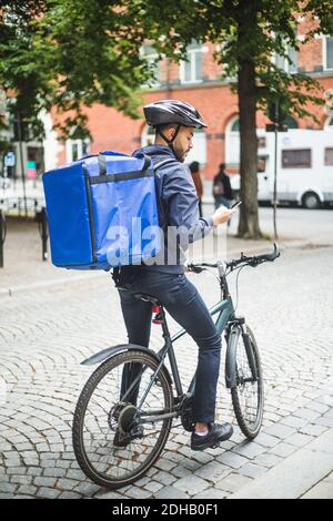 Food delivery man with bicycle using smart phone on street in city Stock Photo