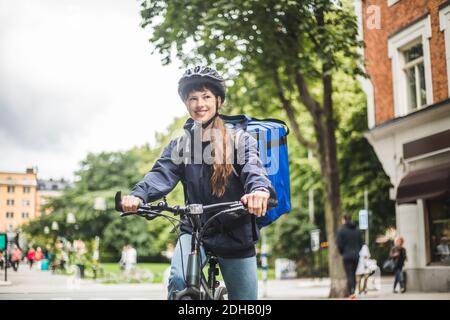 Smiling food delivery woman with bicycle on street in city Stock Photo