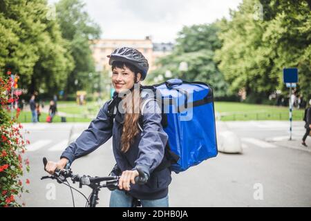 Portrait of smiling food delivery woman with bicycle on street in city Stock Photo