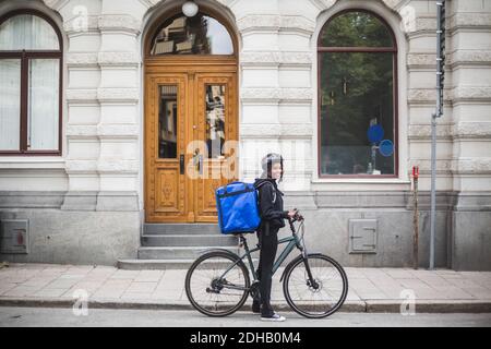 Side view portrait of smiling delivery woman with bicycle on street in city Stock Photo