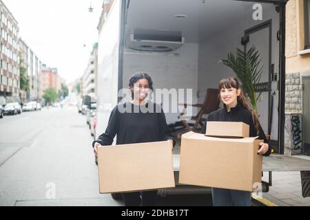 Portrait of smiling female movers unloading boxes from truck on street in city Stock Photo