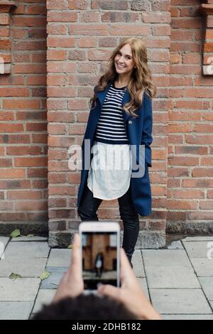 Cropped hands of young man photographing fashionable woman standing against brick wall Stock Photo