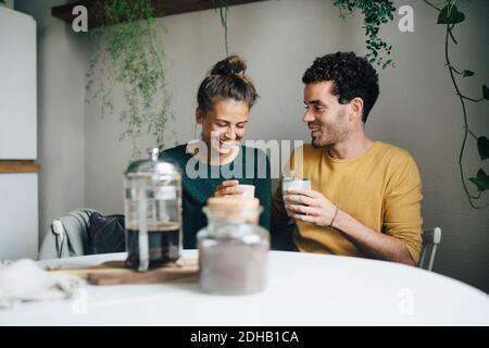 Smiling boyfriend and girlfriend having coffee at table in living room Stock Photo