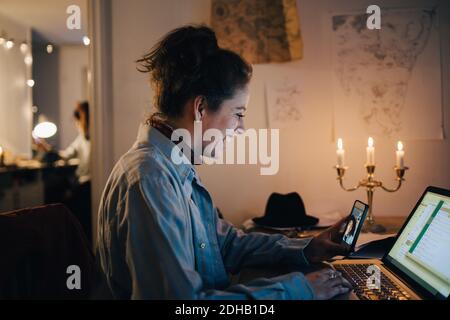 Smiling female engineer video conferencing on mobile phone while using laptop at desk Stock Photo
