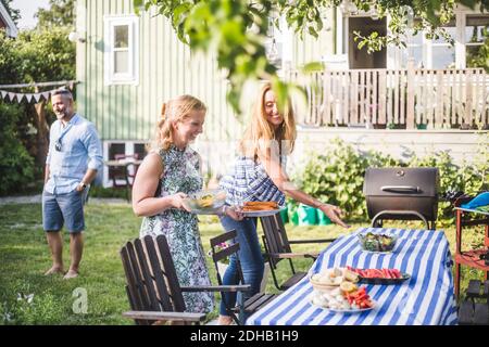 Female friends arranging food on table for social gathering in backyard during summer weekend Stock Photo