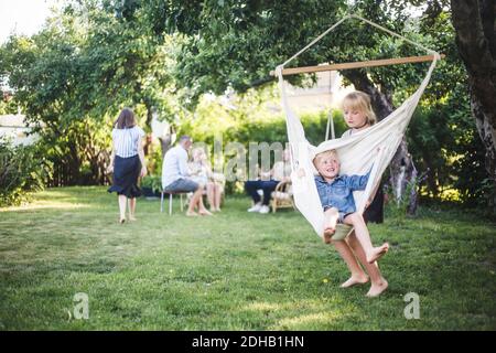 Sister pushing happy boy on swing in backyard Stock Photo