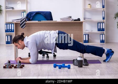 Young handsome male employee doing exercises in the office Stock Photo