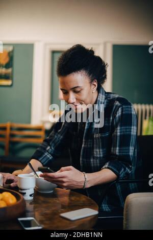 Smiling businessman using mobile phone while having food at table in creative office Stock Photo