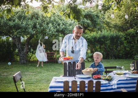 Mature father directing son with food plate while pointing at table in yard Stock Photo