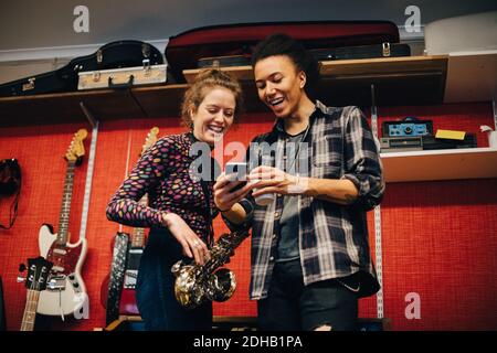 Woman with saxophone looking at man using smart phone while practicing at recording studio Stock Photo