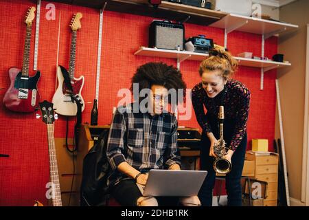 Woman with saxophone looking at man using laptop while practicing at recording studio Stock Photo