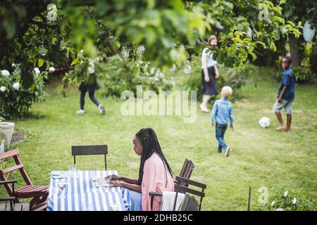 Woman working on laptop while children playing in backyard Stock Photo