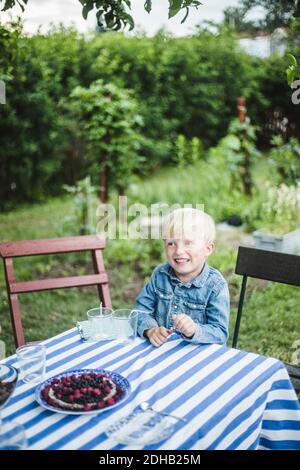 Smiling boy looking away while sitting at dining table in backyard Stock Photo