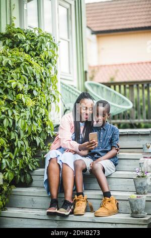 Full length of happy mother and son looking at smart phone while sitting on steps Stock Photo