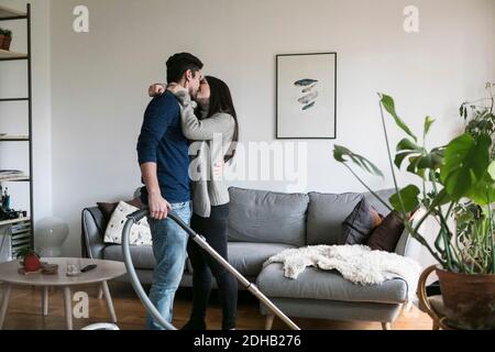 Couple kissing while cleaning living room at home Stock Photo