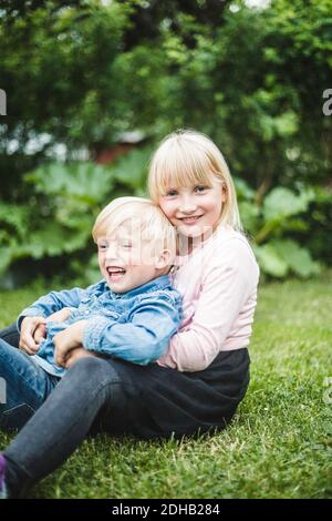 Happy brother and sister sitting together on grassy field Stock Photo